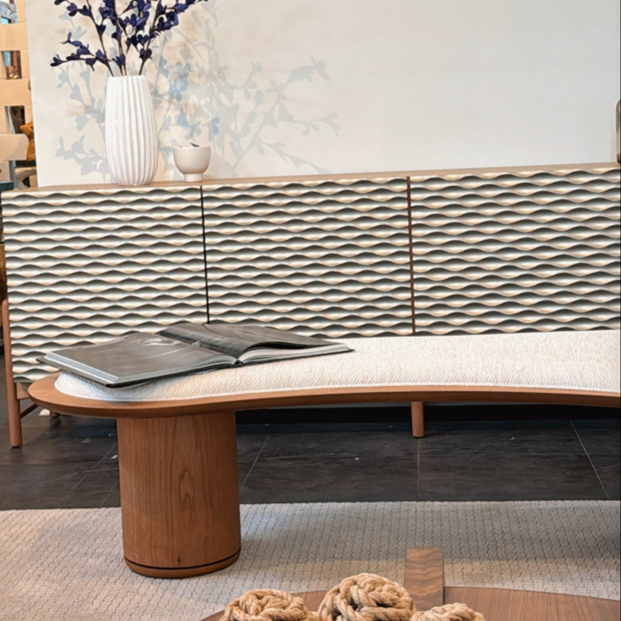 Modern living room with a curved wooden bench, decorative items, and a textured wall.