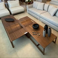 Load image into Gallery viewer, A modern coffee table with a minimalist metal base and a wooden surface featuring a unique curved detail in a living room setting.