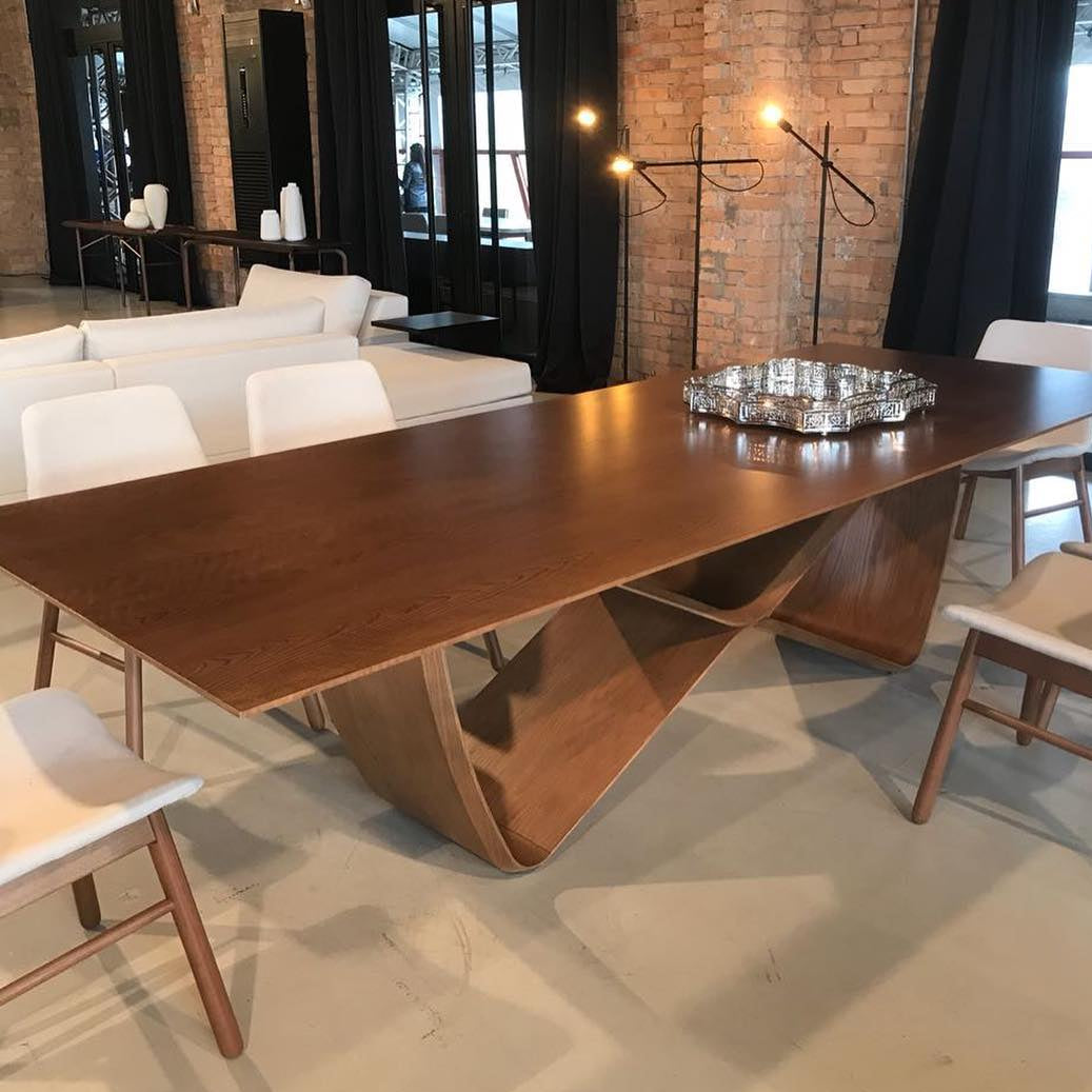 A modern dining table with a unique infinity symbol shaped base and a wooden tabletop.