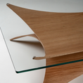 Load image into Gallery viewer, Close-up of a modern wooden table featuring a curved, wave-like oak wood top with a clear glass shelf supported by small metal brackets.