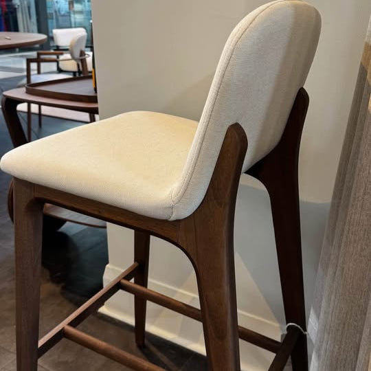 Bar stool with white cushioned seat and backrest in a room setting.