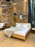 Load image into Gallery viewer, Wooden bed with white bedding in a room with woven walls and decorative branches.