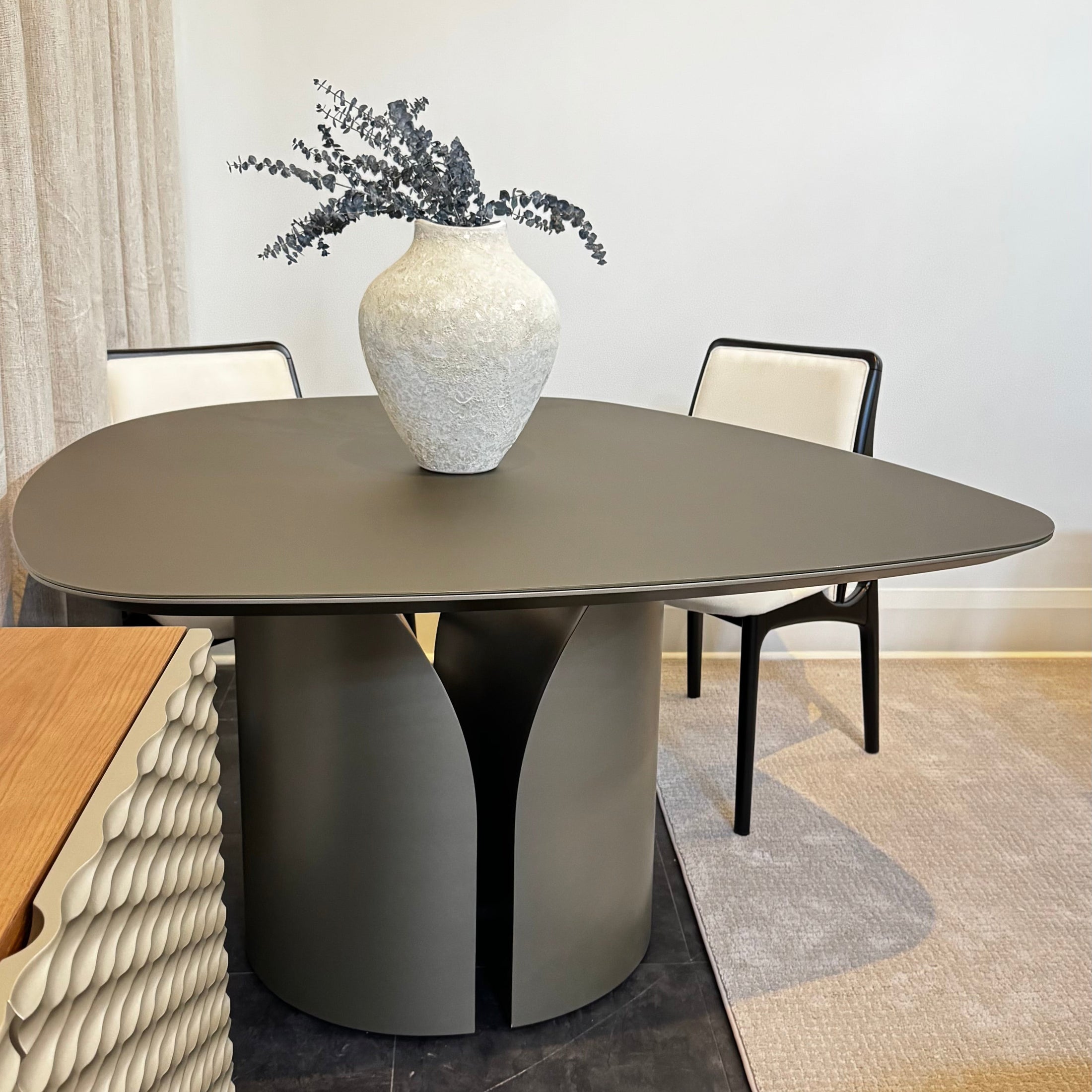 Modern dining table with a vase of flowers in a room with chairs and decor.