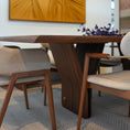 Charger l'image dans la visionneuse de la galerie, A modern dining table with a sculptural dark wood base and matching upholstered chairs, styled in a contemporary dining room with a large abstract gold wall art piece behind it.