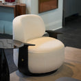 Load image into Gallery viewer, A modern round upholstered armchair in textured off-white fabric with black curved armrests and a black circular base, shown in a styled interior setting.