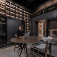 Load image into Gallery viewer, Person sitting at a table in a modern, dimly lit room with wooden shelves and decor.