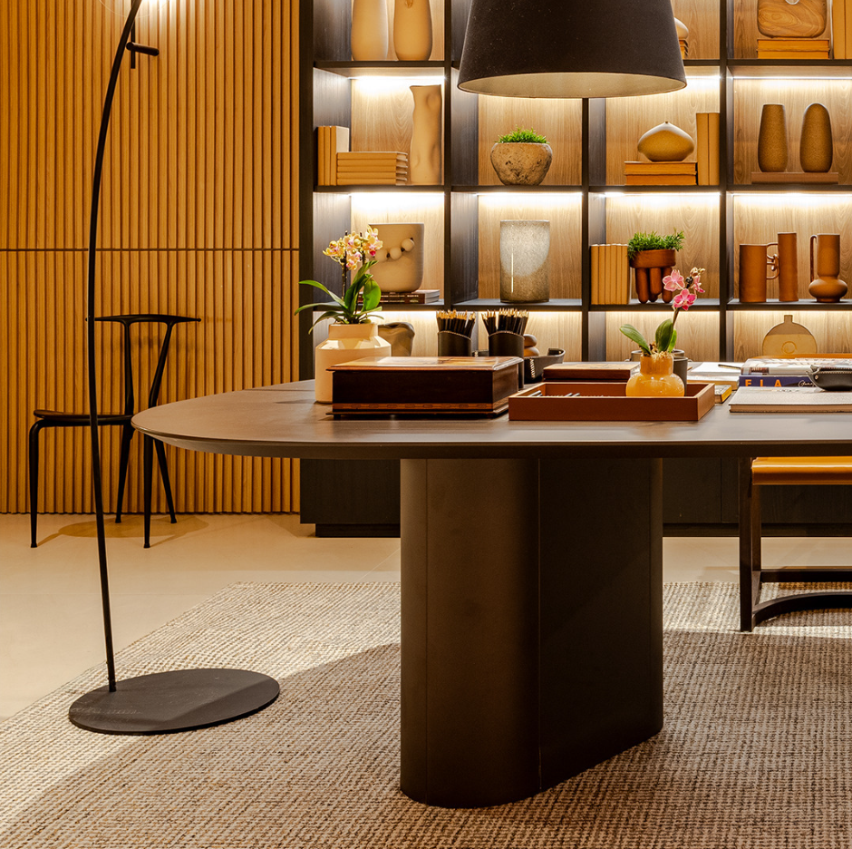 A contemporary design dining table with a smooth, oval-shaped wood tabletop in graphite color, supported by two cylindrical legs.