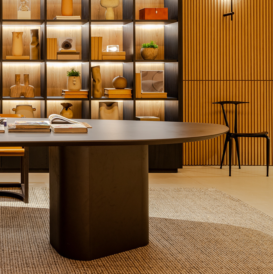 A contemporary design dining table with a smooth, oval-shaped wood tabletop in graphite color, supported by two cylindrical legs.