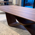 Load image into Gallery viewer, A modern dining table with a unique infinity symbol shaped base and a wooden tabletop.