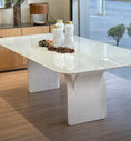 Load image into Gallery viewer, Modern white dining table with decorative items in a room with wooden flooring and a large window.