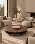 Charger l'image dans la visionneuse de la galerie, A modern round wooden coffee table with a dark wood grain top and a travertine marble center pedestal, styled in a warm, contemporary living room with beige armchairs and textured rugs.