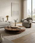 Charger l'image dans la visionneuse de la galerie, A modern living room scene featuring a round walnut coffee table on a textured light rug, next to a gray upholstered armchair and a light gray sofa with a gold table lamp.