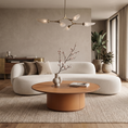 Load image into Gallery viewer, A modern living room featuring a curved white sofa, a round wooden coffee table, a textured beige rug, and large windows with beige curtains.