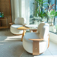 Load image into Gallery viewer, Modern white chairs with wooden legs in a bright room with large windows and plants.

