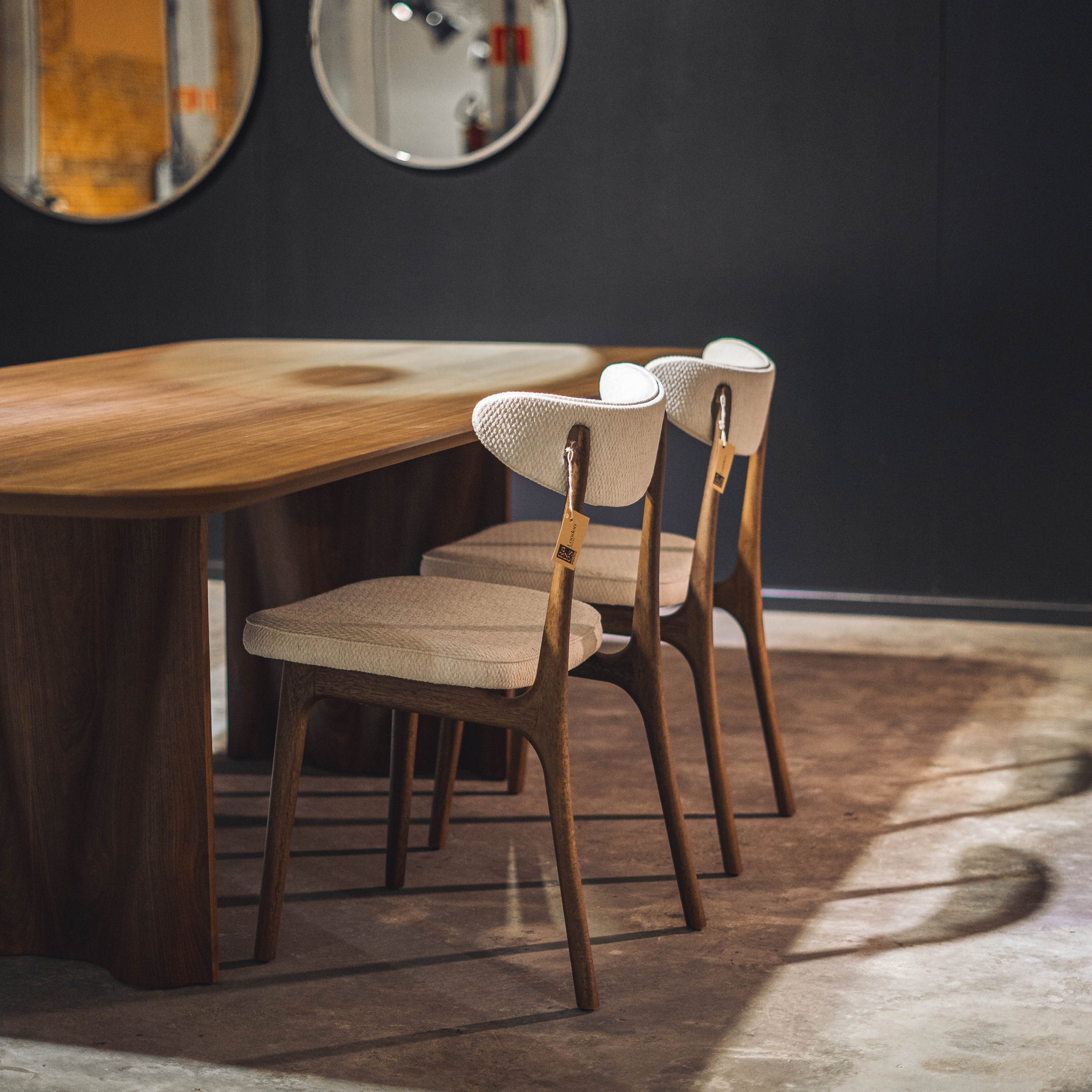 Dining area with wooden table and chairs against a dark wall with two round mirrors.