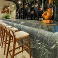 Load image into Gallery viewer, Bar area with marble counter, wooden stools, and wine bottles on shelves.
