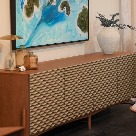 A mid-century modern sideboard cabinet with a textured geometric patterned front, styled in a room setting under a framed abstract painting.