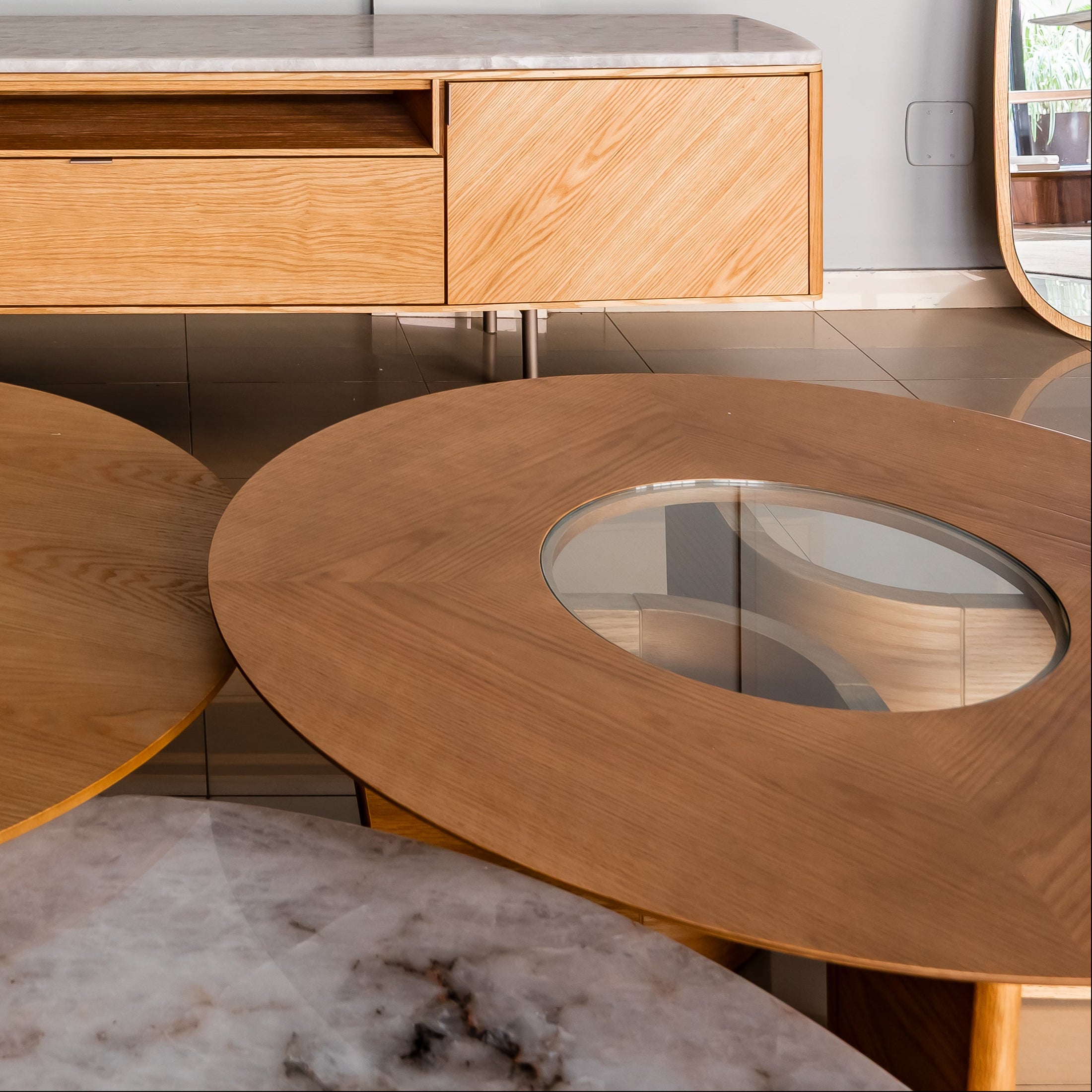 Wooden entertainment console against a light gray wall with two round wooden tables in front.