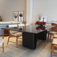 Load image into Gallery viewer, Modern dining room with a black glass table and wooden chairs.
