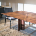 Load image into Gallery viewer, Wooden dining table with chairs in a room with large windows.
