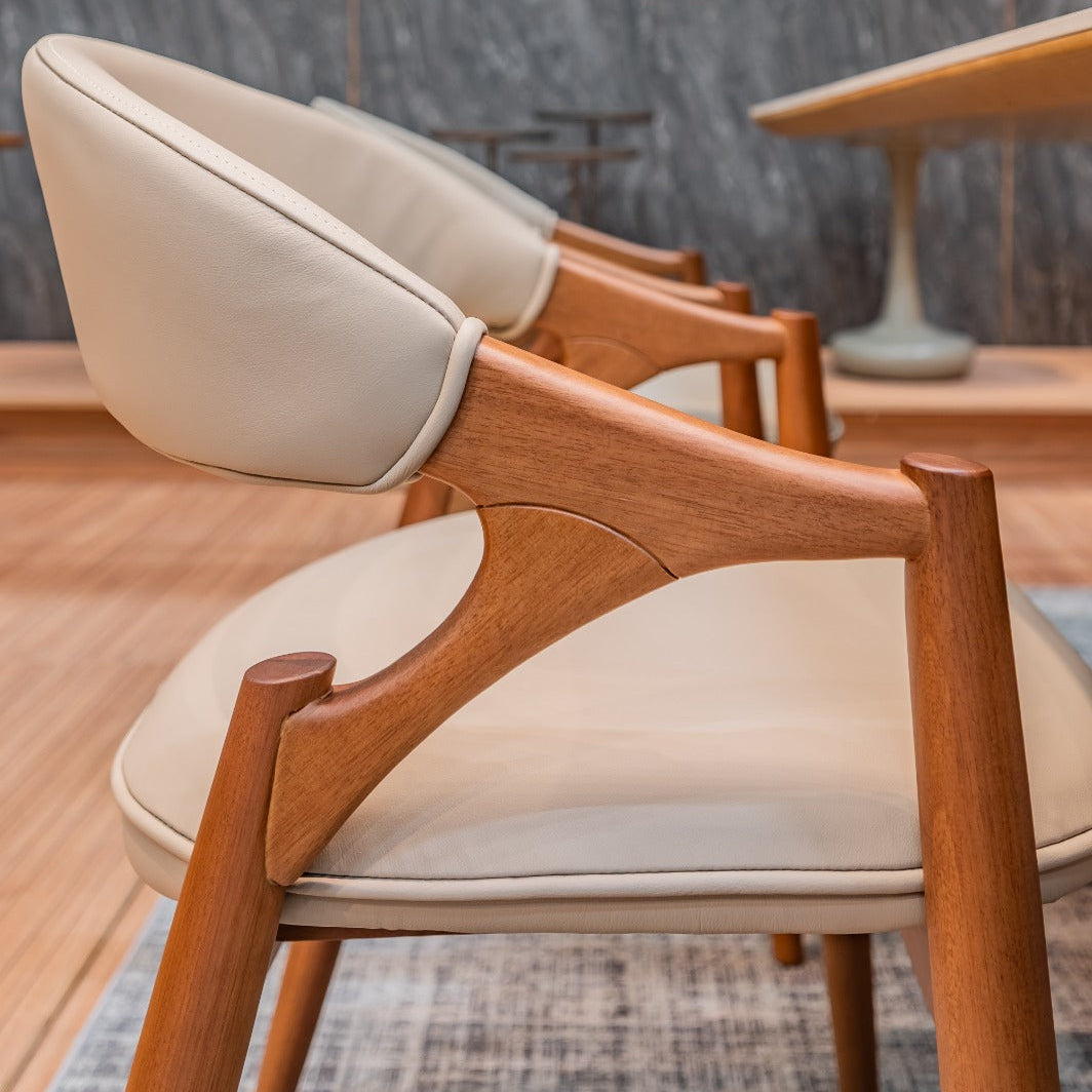Wooden chairs with white cushions in a room with a textured wall and table.