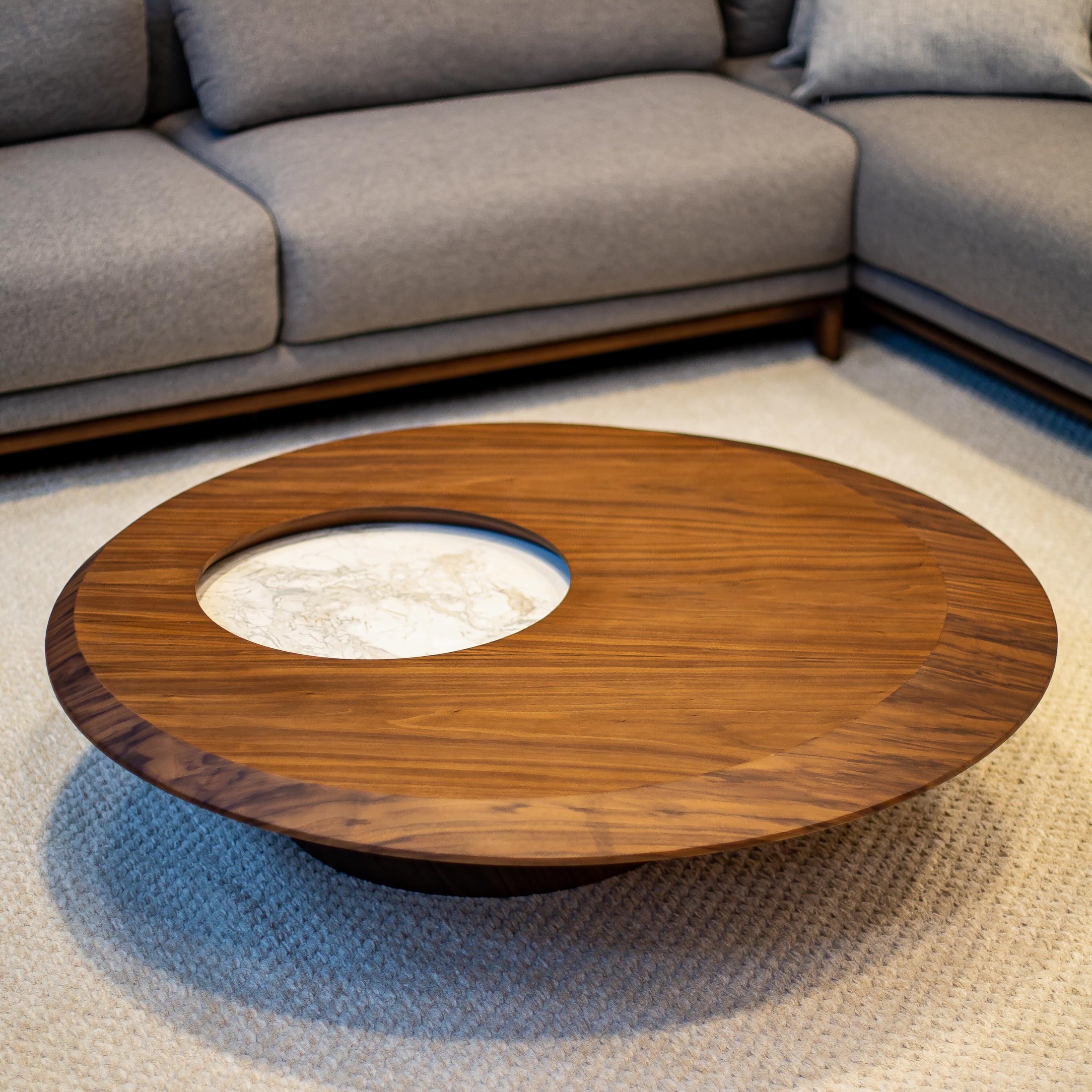 Round wooden coffee table in a living room with a gray sectional sofa.