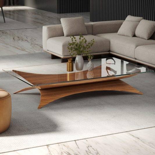 A modern coffee table with a curved wooden base and a clear glass top, styled in a contemporary living room setting with a beige sectional sofa and marble flooring.